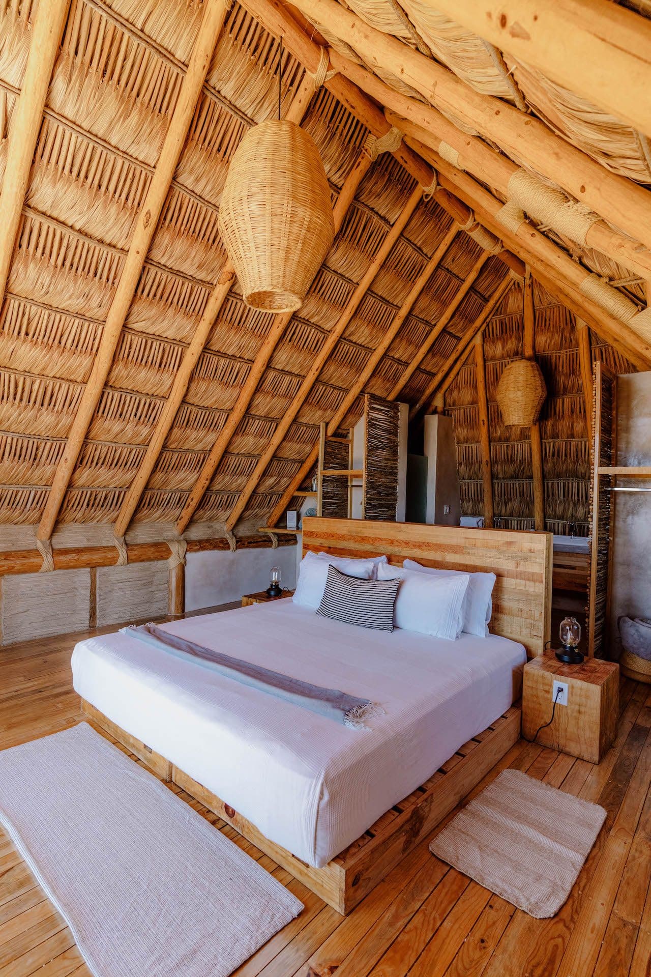 A guest room with a low wooden bed under a thatched palapa roof